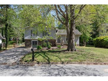Charming split-level home featuring stone accents, a well-maintained lawn, and a mature shade tree at 8876 Ashwood Dr, Riverdale, GA 30274