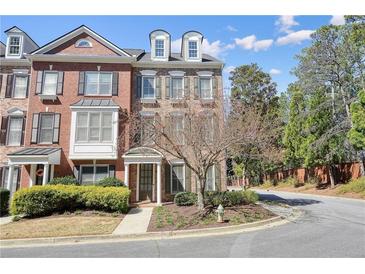 Brick townhome featuring manicured landscaping, a walkway, and a charming entrance, all under a bright, partly cloudy sky at 4406 Kendall Way, Roswell, GA 30075