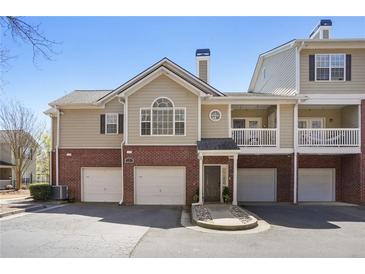 Charming townhouse featuring a two-car garage, brick accents, and well-maintained landscaping on a sunny day at 7104 Woodland Ln, Alpharetta, GA 30009