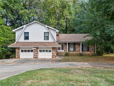 Charming split-level home featuring a two-car garage and partially bricked exterior with lots of mature trees at 235 Shallowford Nw Rd, Kennesaw, GA 30144
