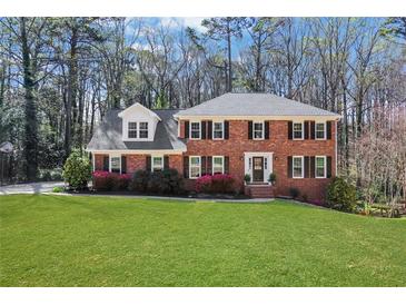 Charming two-story brick home with a manicured lawn, black shutters, and blossoming flower beds at 1135 Parkview Sw Way, Lilburn, GA 30047