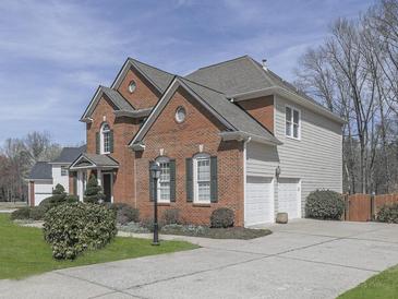 Side view of a beautiful brick and vinyl two-story home with an attached two car garage, manicured bushes, and a concrete driveway at 3891 Greensward Nw Vw, Kennesaw, GA 30144