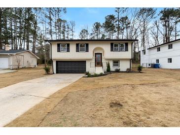 Charming split-level home with a dark garage door, manicured lawn, and neatly trimmed bushes at 6660 Hidden Brook Trl, Atlanta, GA 30349