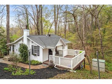 Charming cottage-style home with white exterior, a deck, and mature trees in a wooded setting at 106 Maple St, Roswell, GA 30075