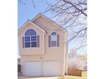 Two-story home features a two-car garage, light siding, updated windows, and mature trees surrounding the property at 116 Ventura Trl, Stockbridge, GA 30281