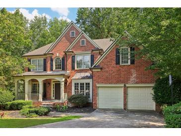 Charming brick home with a welcoming front porch and a two-car garage nestled among mature trees at 8355 Ainsworth Dr, Cumming, GA 30041
