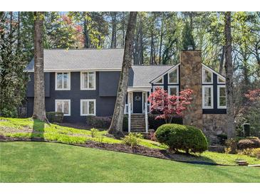 Charming two-story home with dark siding, a stone chimney, mature trees, and a lush green lawn at 11630 Mountain Laurel Dr, Roswell, GA 30075