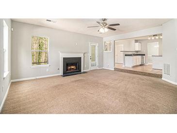 Spacious living room with fireplace, ceiling fan, and open access to kitchen area at 498 Pecan Wood Cir, Fairburn, GA 30213