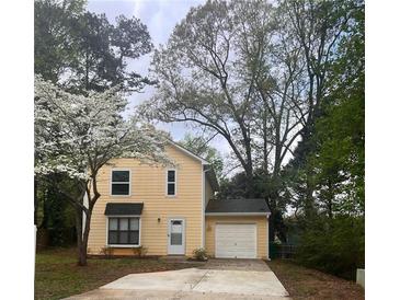 Charming two-story home with a light yellow exterior, attached garage and driveway, surrounded by beautiful trees at 5331 Ridge Forest Dr, Stone Mountain, GA 30083
