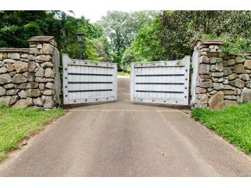 A stone and wood entrance gate leads to a private estate drive surrounded by mature trees at 2100 West Wesley Rd, Atlanta, GA 30327