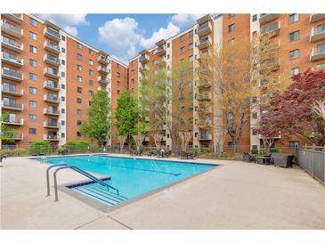 Outdoor pool surrounded by chairs and trees in front of a brick apartment building on a partly cloudy day at 300 Johnson Ferry Ne Rd # A1008, Atlanta, GA 30328