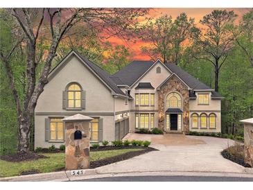 Stunning two-story stucco home featuring a stone accent wall, manicured lawn, and driveway leading to the three-car garage at 545 Slane Trce, Roswell, GA 30076
