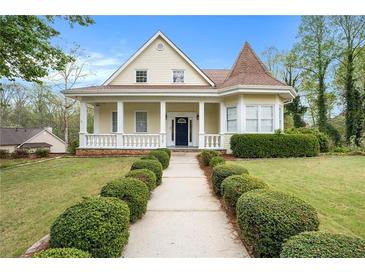 Charming yellow two-story home featuring a manicured lawn, front porch, and unique architectural details at 5732 Falls View Dr, Buford, GA 30518