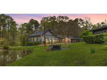 Charming home featuring a well-manicured lawn, mature trees, and a serene pond, perfect for outdoor enjoyment at 6585 Queen Mill Se Rd, Mableton, GA 30126