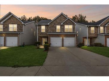 Charming townhome exterior featuring stone accents and a two-car garage, set against a twilight sky at 8849 Seneca Rd, Palmetto, GA 30268
