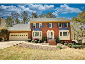 Charming red brick two-story home with blue shutters, bay windows and a well-manicured lawn and landscaping at 4814 Riveredge Cv, Snellville, GA 30039