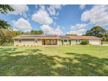 Charming single-story home with solar panels, stone accents, covered front porch, and a spacious, well-manicured front lawn at 3557 Bill Gardner Pkwy, Locust Grove, GA 30248