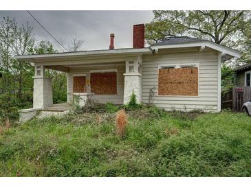 Overgrown front yard of boarded-up bungalow-style home with a brick chimney and covered porch at 1366 Sylvan Sw Rd, Atlanta, GA 30310