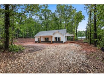 Charming, newly built single-story home with light gray roof, light siding and gravel driveway surrounded by trees at 1765 Harmony Rd, Temple, GA 30179