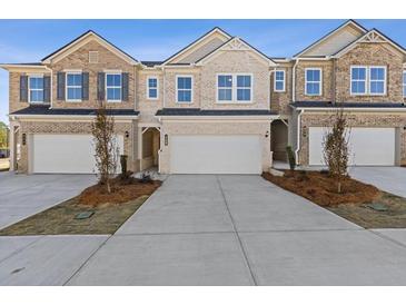 Charming townhome exterior features a two-car garage, brick facade, and well-manicured landscaping at 936 Elwood St, Dacula, GA 30019