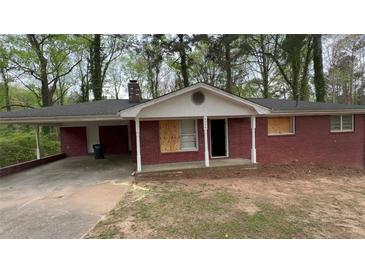 Charming brick home featuring a carport and a well-maintained yard; windows are boarded at 6344 Fitzgerald Ln, Austell, GA 30168