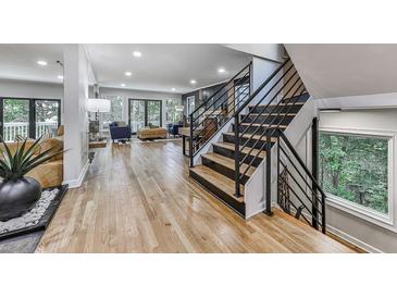 Bright foyer boasts hardwood floors, staircase with black metal railings, and view to living room with backyard access at 120 Huntcliff Pt, Atlanta, GA 30350