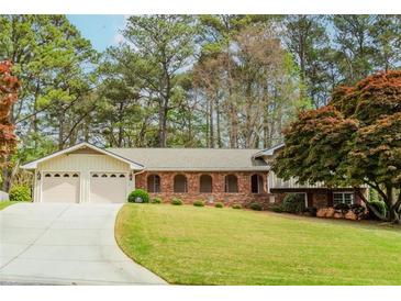 Charming single story brick home with a well-manicured lawn, mature trees, and attached two-car garage at 1152 Old Coach Rd, Stone Mountain, GA 30083