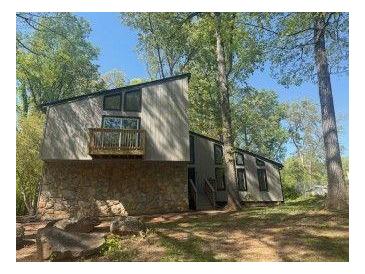 Unique, modern home with stone facade, small balcony, and large windows surrounded by mature trees at 3684 Big Springs Rd, Decatur, GA 30034
