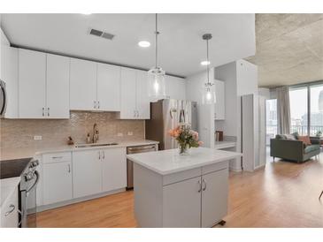 Bright kitchen features white cabinets, stainless appliances, an island, and views of the living area at 860 Peachtree Ne St # 1103, Atlanta, GA 30308