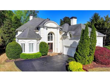 Elegant white home featuring arched windows, manicured landscaping, and a paved driveway at 7080 Greatwood Trl, Alpharetta, GA 30005