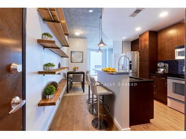Modern kitchen features wood floors, floating shelves, a granite breakfast bar, and stainless steel appliances at 860 Peachtree Ne St # 1010, Atlanta, GA 30308