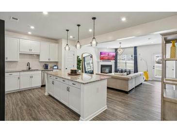 Open-concept living room with white cabinets, granite counters, and island with pendant lighting, flowing into a cozy living area at 375 Crider Ct, Woodstock, GA 30188