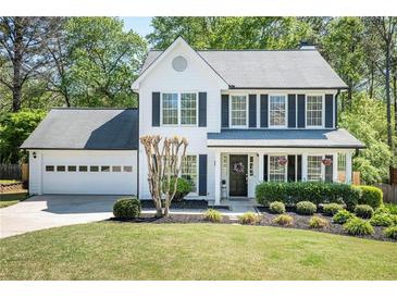 Charming two-story home boasts a manicured lawn, attached garage and a welcoming front porch with blooming flowers at 12495 Concord Hall Dr, Alpharetta, GA 30005