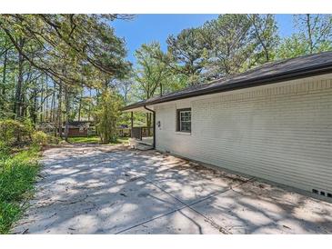 Side view of home featuring a white brick wall, large driveway, and surrounding trees at 1679 Hollyhock Ter, Decatur, GA 30032
