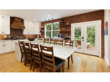 Bright kitchen features a long island with a stone countertop, white cabinetry, stainless appliances, and brick accent wall at 6765 Creek View Ln, Cumming, GA 30041