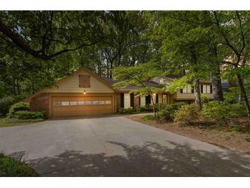 Charming home featuring an attached garage and a well-manicured lawn with beautiful mature trees at 2343 Kings Point Dr, Dunwoody, GA 30338