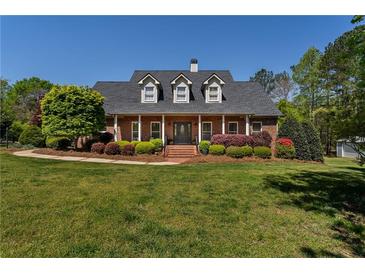 Charming brick home boasts a manicured lawn and lush landscaping with a covered front porch and dormer windows at 200 Sugar Mill Ln, Canton, GA 30115
