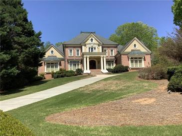 Stately brick home features manicured lawn, mature trees, and a welcoming facade with classic architectural details at 9390 Colonnade Trl, Johns Creek, GA 30022