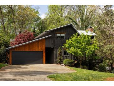 Contemporary home featuring black and wood siding, attached garage, and beautifully landscaped yard with mature trees at 4727 Emily Sw Dr, Lilburn, GA 30047