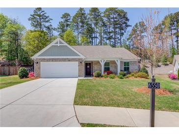 Charming single-story home featuring a well-manicured lawn, brick facade, and a welcoming front porch with a bench at 6550 Lantana Village Way, Cumming, GA 30028