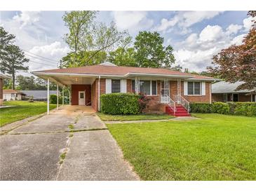 Charming brick home featuring a well-maintained lawn, covered carport, and landscaped front yard at 5295 Woodland Dr, Lake City, GA 30260
