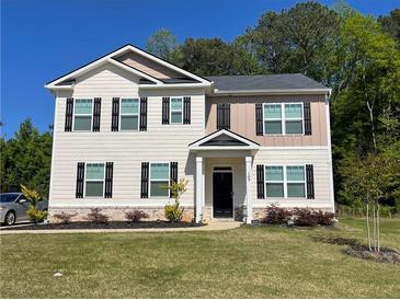 Charming two-story home featuring a manicured lawn and classic black shutters against a light beige and tan facade at 205 Sullivan St, Hampton, GA 30228