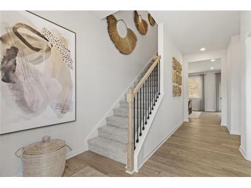 Bright foyer with staircase featuring gray carpet, black railings and light wood trim, leading to the upper level at 8511 Polston Place- Lot 138, Douglasville, GA 30134