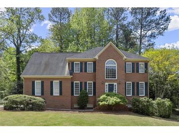 Charming two-story brick home featuring a manicured lawn, lush landscaping, and dark green shutters at 2130 Federal Rd, Roswell, GA 30075
