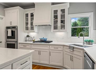 Bright kitchen features white cabinets, stainless steel appliances, and a window overlooking the backyard at 1315 Woodland Trce, Cumming, GA 30041