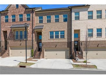 Three-story brick townhouses with attached garages and professional landscaping line the street at 243 Commons Ave, Woodstock, GA 30188