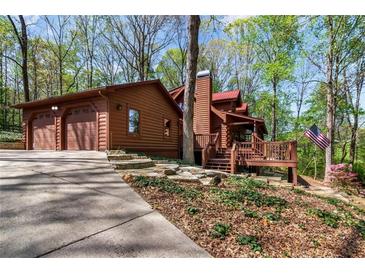 Charming log home with an attached garage, flag and a cozy front porch nestled among mature trees at 6515 Namon Wallace Dr, Cumming, GA 30028