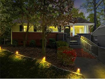 Charming home featuring a cozy porch, brick accents, and professionally landscaped front yard illuminated by landscape lighting at 1211 Argonne Ne Way, Atlanta, GA 30324