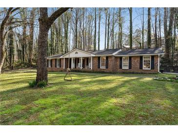 Charming brick home featuring a well-manicured lawn, classic columns, and inviting front porch swing at 1351 Stephens Sw St, Lilburn, GA 30047