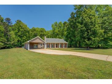 Ranch style home featuring an attached garage and a long concrete driveway on a vast green lawn surrounded by trees at 70 Graystone Dr, Covington, GA 30014